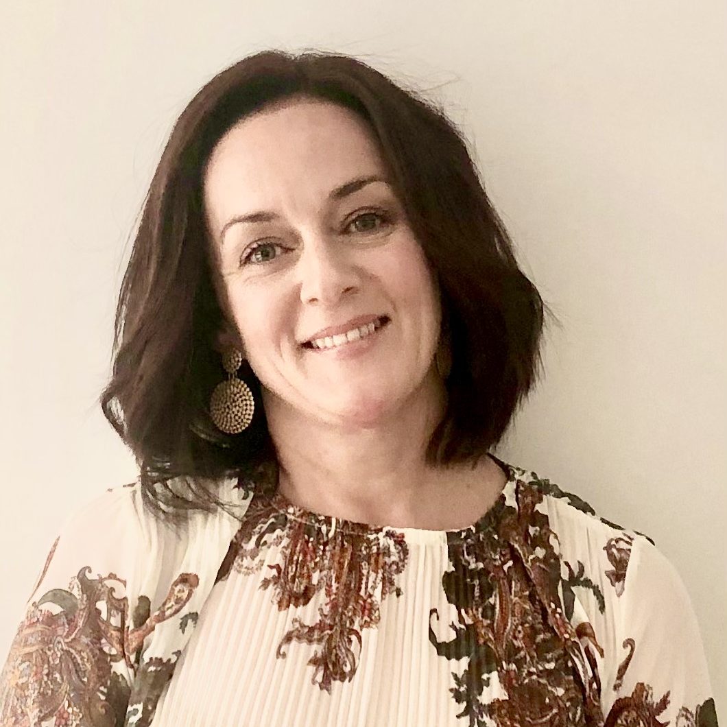 Copywriter and Communications Consultant Kylie O'Driscoll tilts her hear to the right while smiling at the camera. Kylie is wearing rounds gold earrings, and a cream and brown floral top.