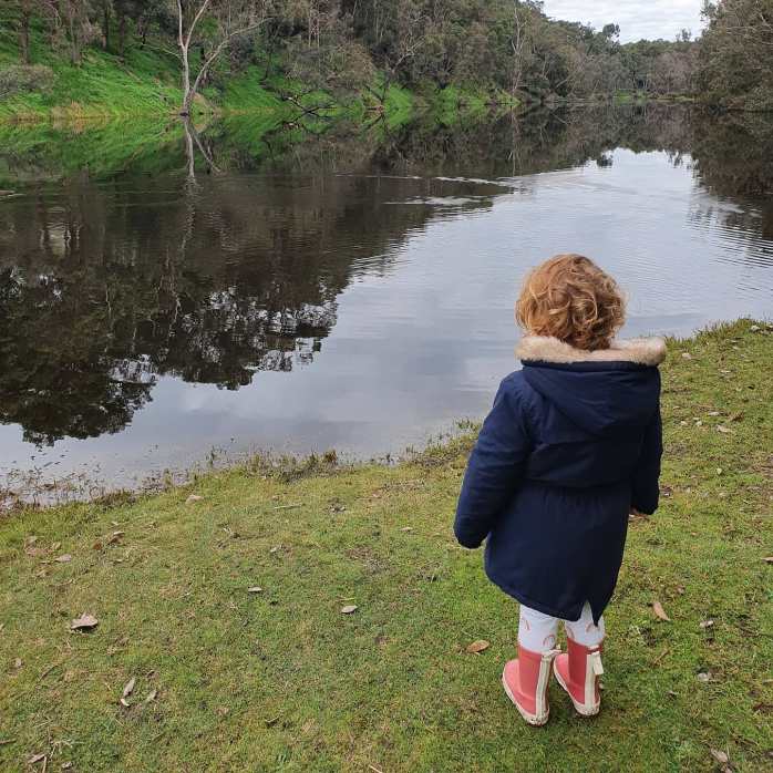 Small girl wearing raincoat and gumboots, standing by a pond