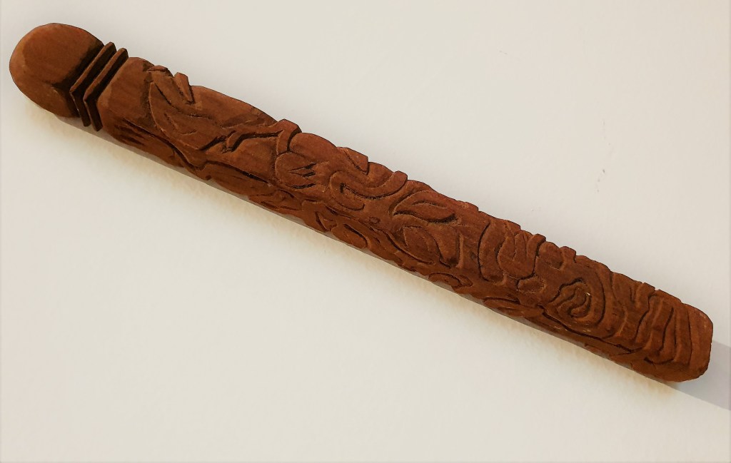 Long, slim, sandalwood carving with intricate paths of branches and vines.