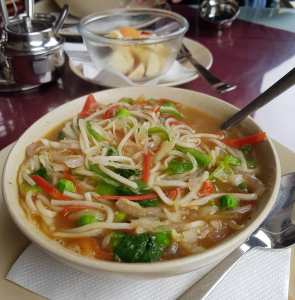 A bowl of Indian broth filled with oodles, peas, capsicum and onions.